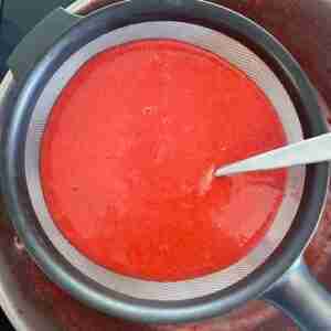 Putting pureed strawberries through a sieve to remove the seeds for homemade strawberry jello..