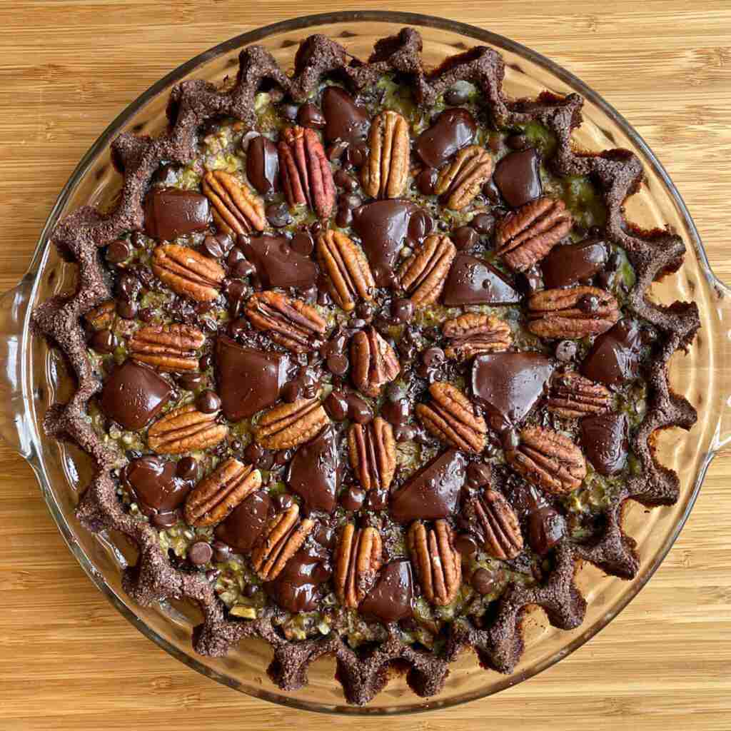 An overhead shot of a low-carb chocolate chip pecan pie decorated with a pattern of sugar-free dark chocolate chunks and pecans.