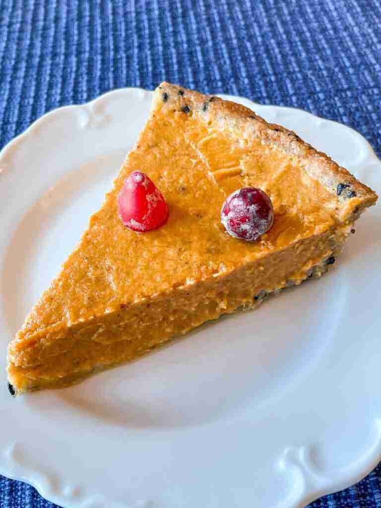 A slice of healthy pumpkin tart made with monk fruit and yogurt and topped with cranberries on a white plate.