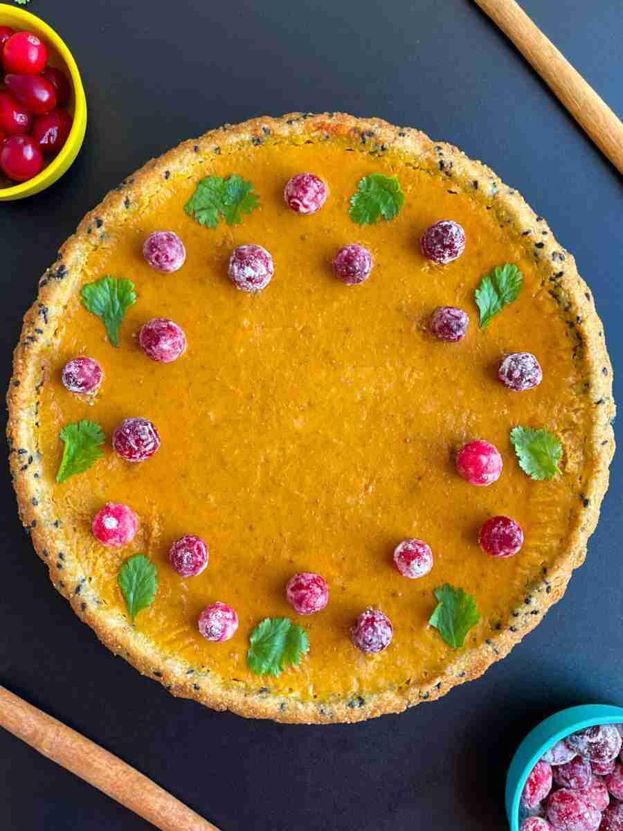 A healthy pumpkin tart in a black sesame, almond flour crust, topped with sugared cranberries.