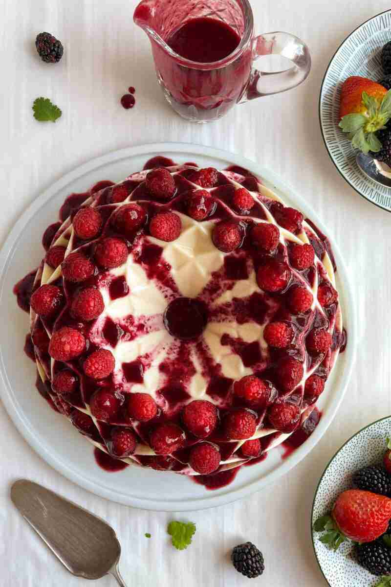 A milk jello cake decorated with raspberries and red berry sauce and made in a Nordic Ware bundt cake pan.