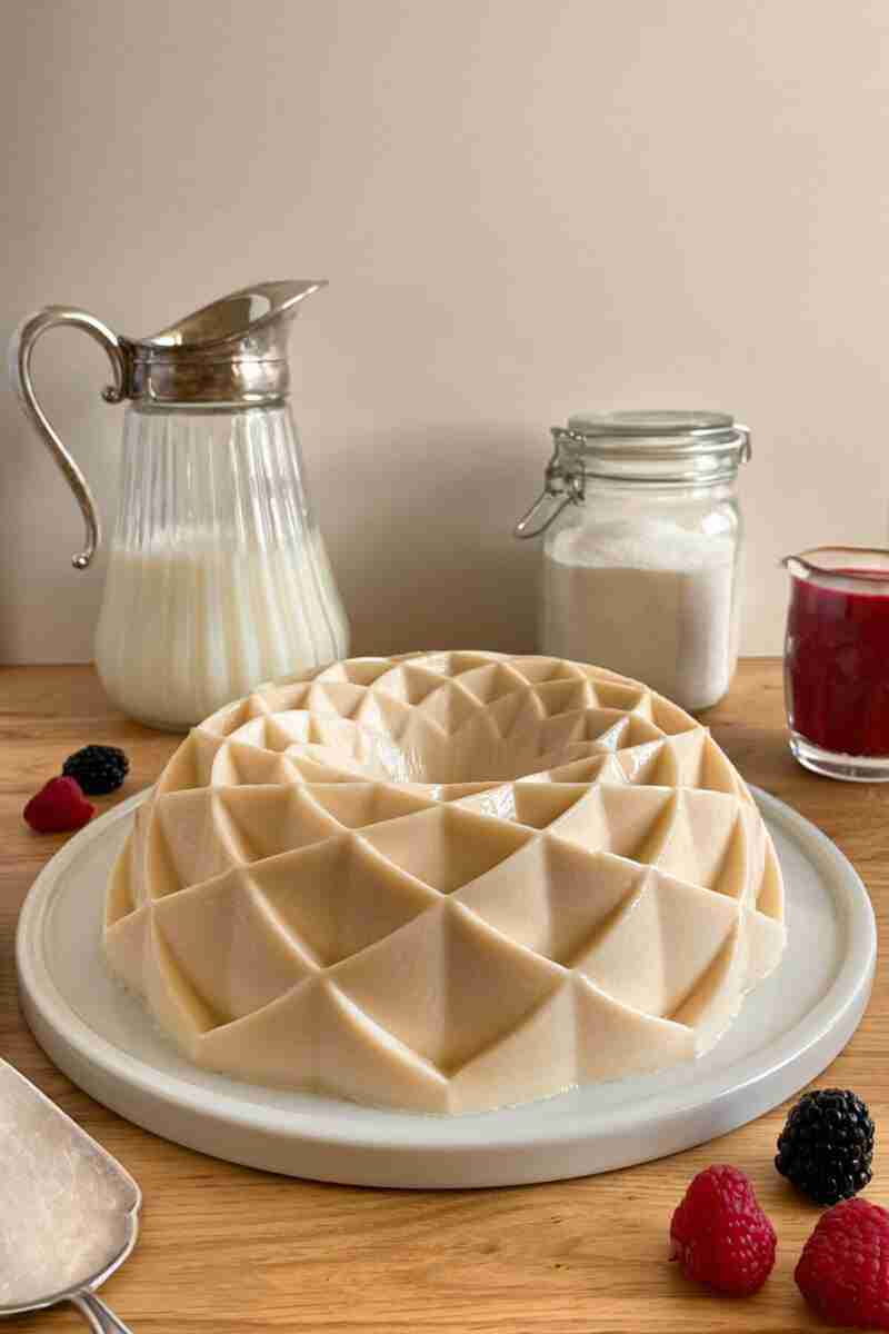 A fresh milk jello cake on the table with a few berries around it.