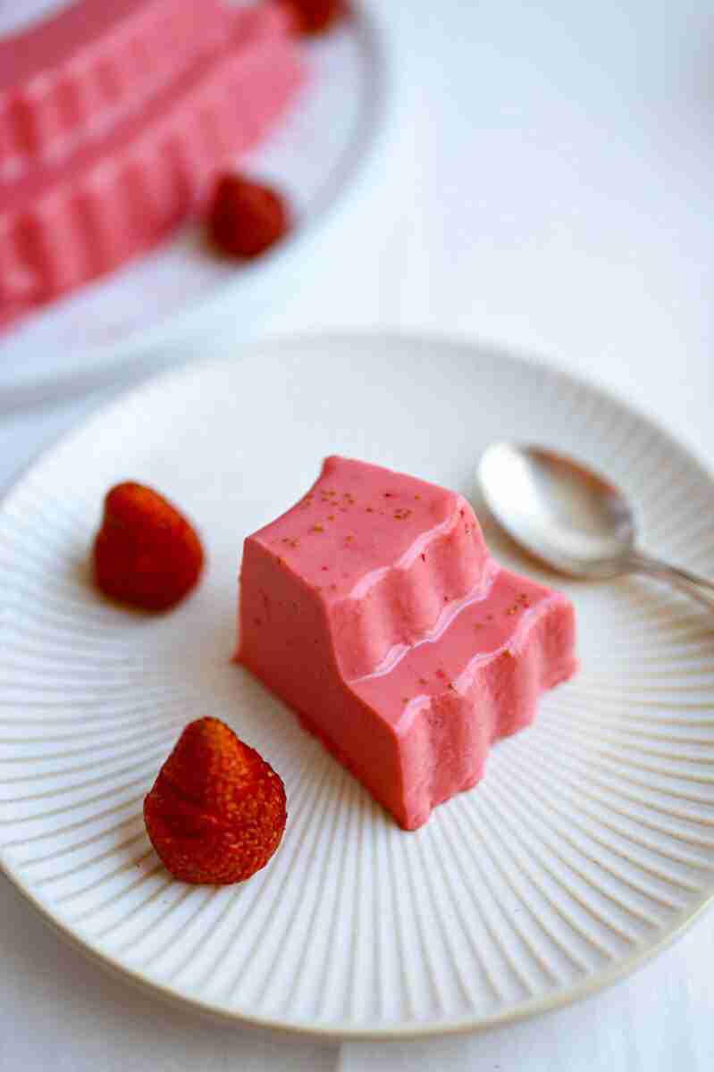 A slice of sugar-free gelatin cake on a plate with a few strawberries next to it.