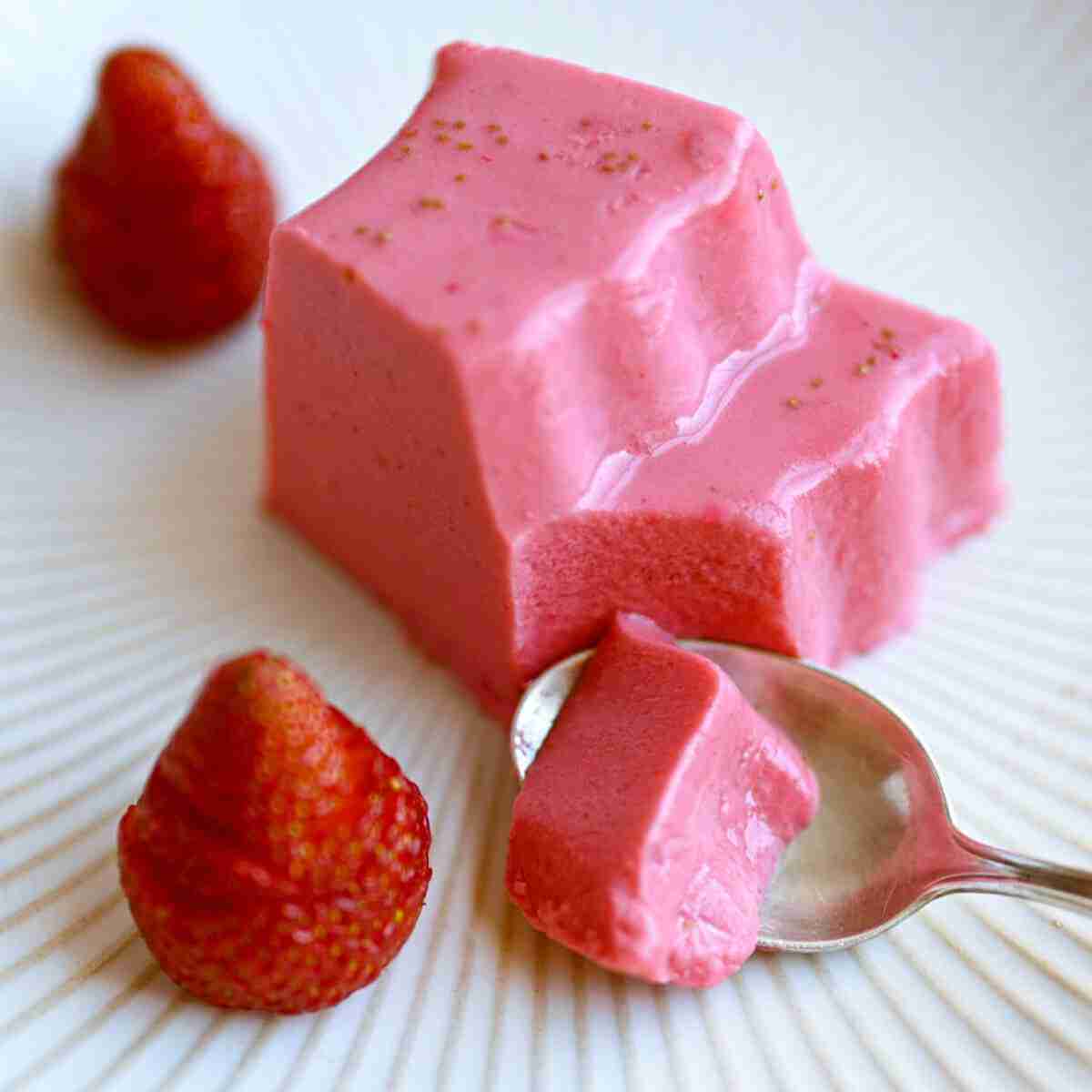 A slice of strawberry milk jello or strawberry milk jelly with 2 strawberries next to it.