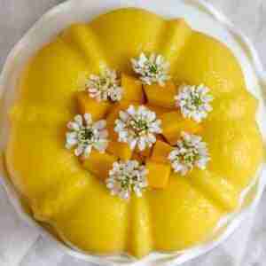 Vegan mango coconut milk jello cake topped with mango slices and fresh white flowers.