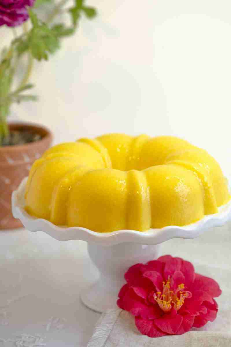 Healthy, tropical, vegan mango coconut milk jello cake made in a bundt cake pan and displayed on a cake pedestal.