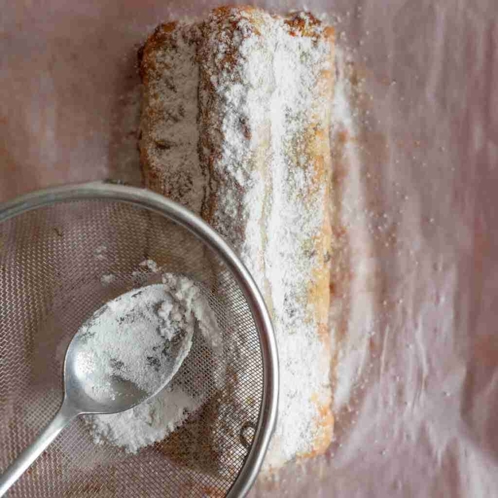 A step in the recipe: Using a sieve to sprinkle powdered sugar on the almond flour Stollen.