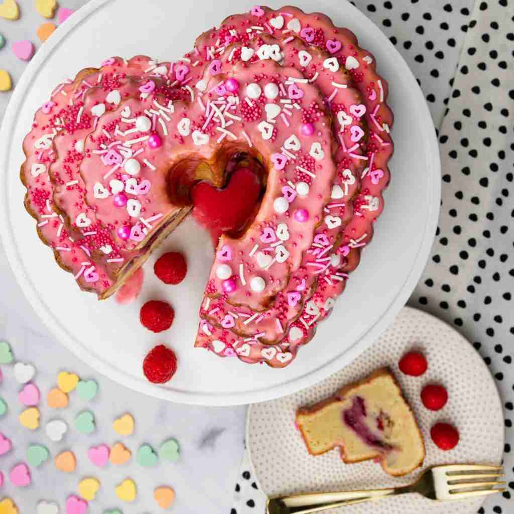 A raspberry swirl bundt cake with fresh raspberries and white and pink Valentine's Day sprinkles.