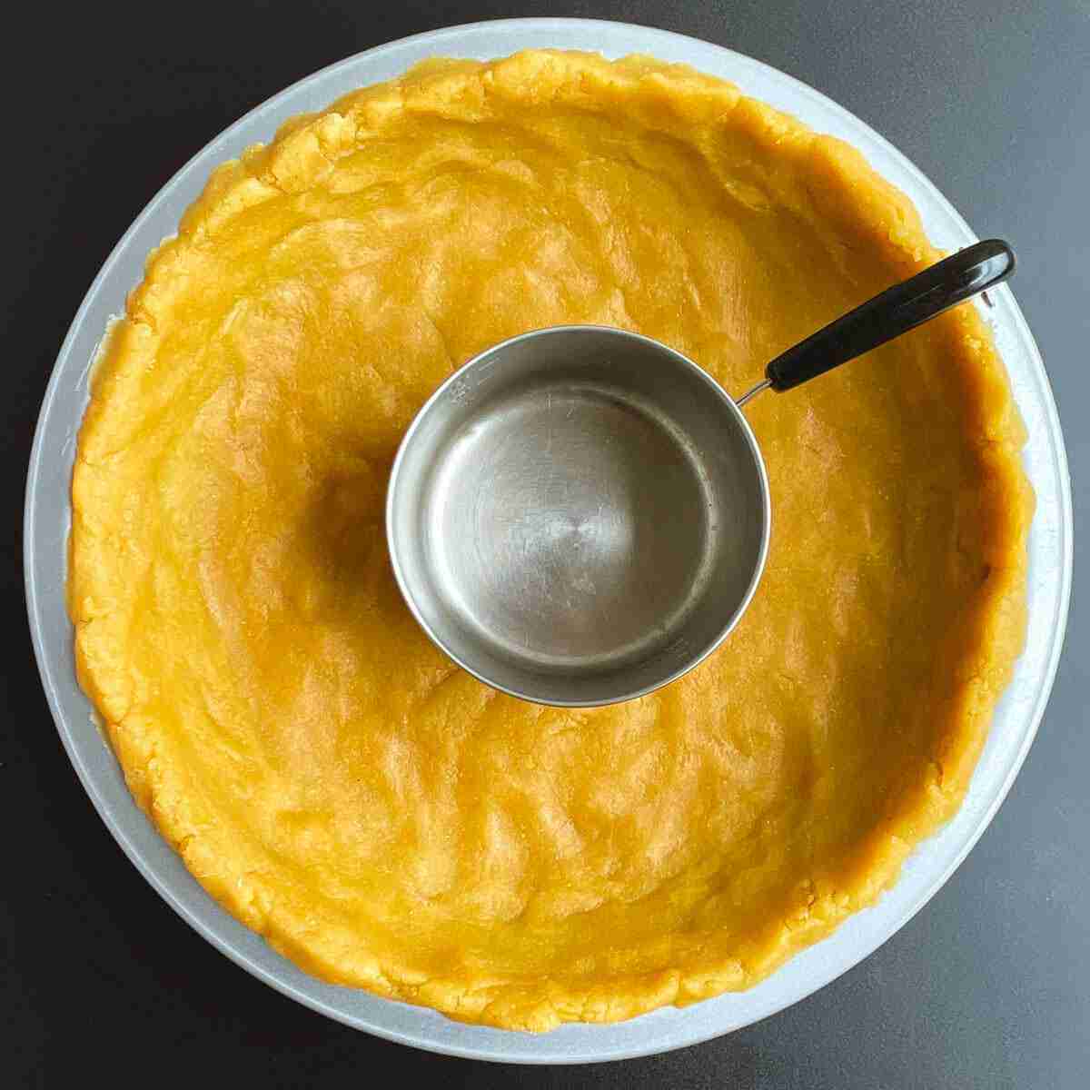 The image illustrates how to use a mini saucepan to flatten the bottom of the chickpea quiche crust and build the sides.
