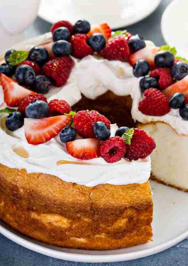 Keto Angel Food Cake topped with whipped cream, fresh raspberries, strawberries, blueberries, mint leaves.