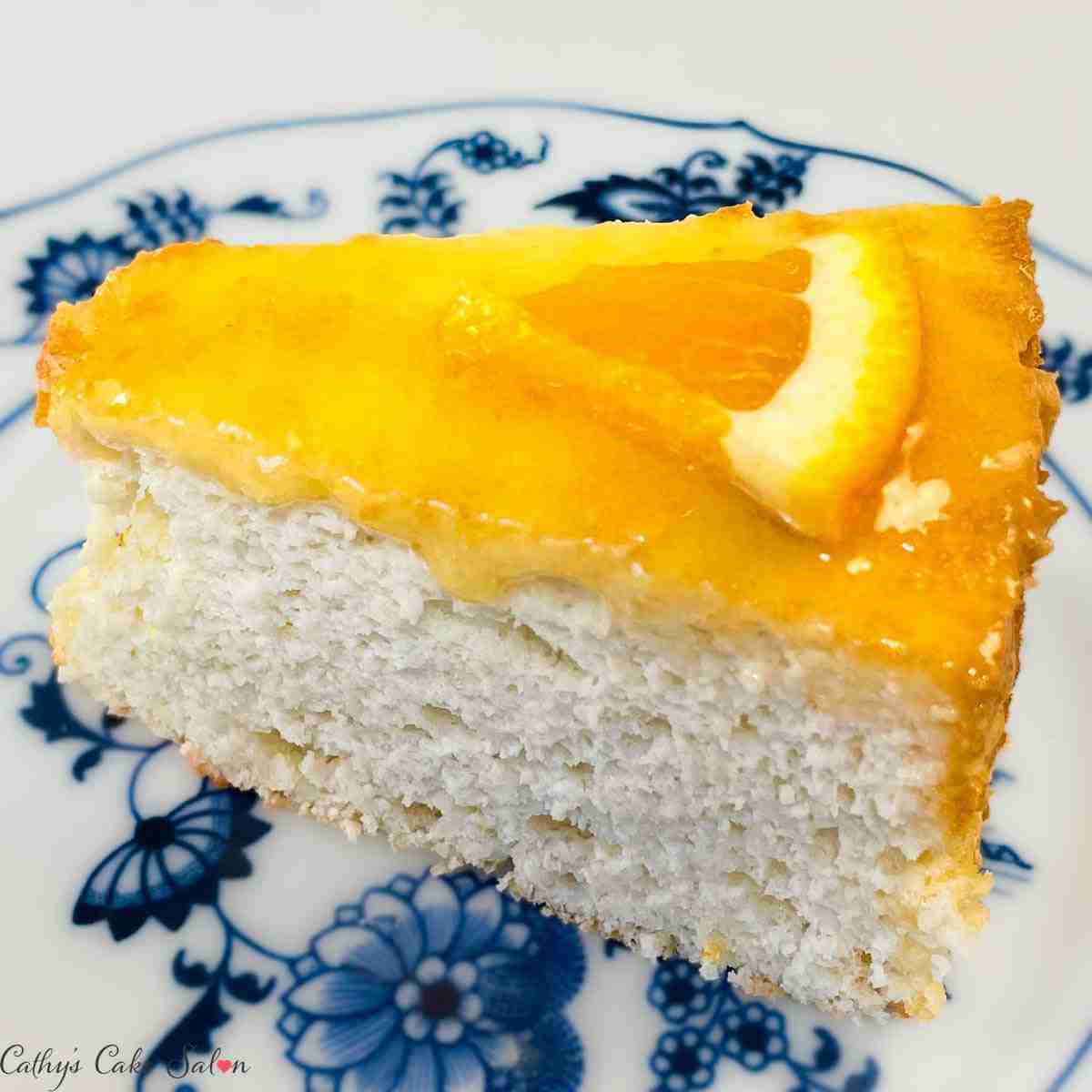 A slice of keto orange cake, an orange angel food cake, topped with sugar free orange glaze and a slice of fresh orange.