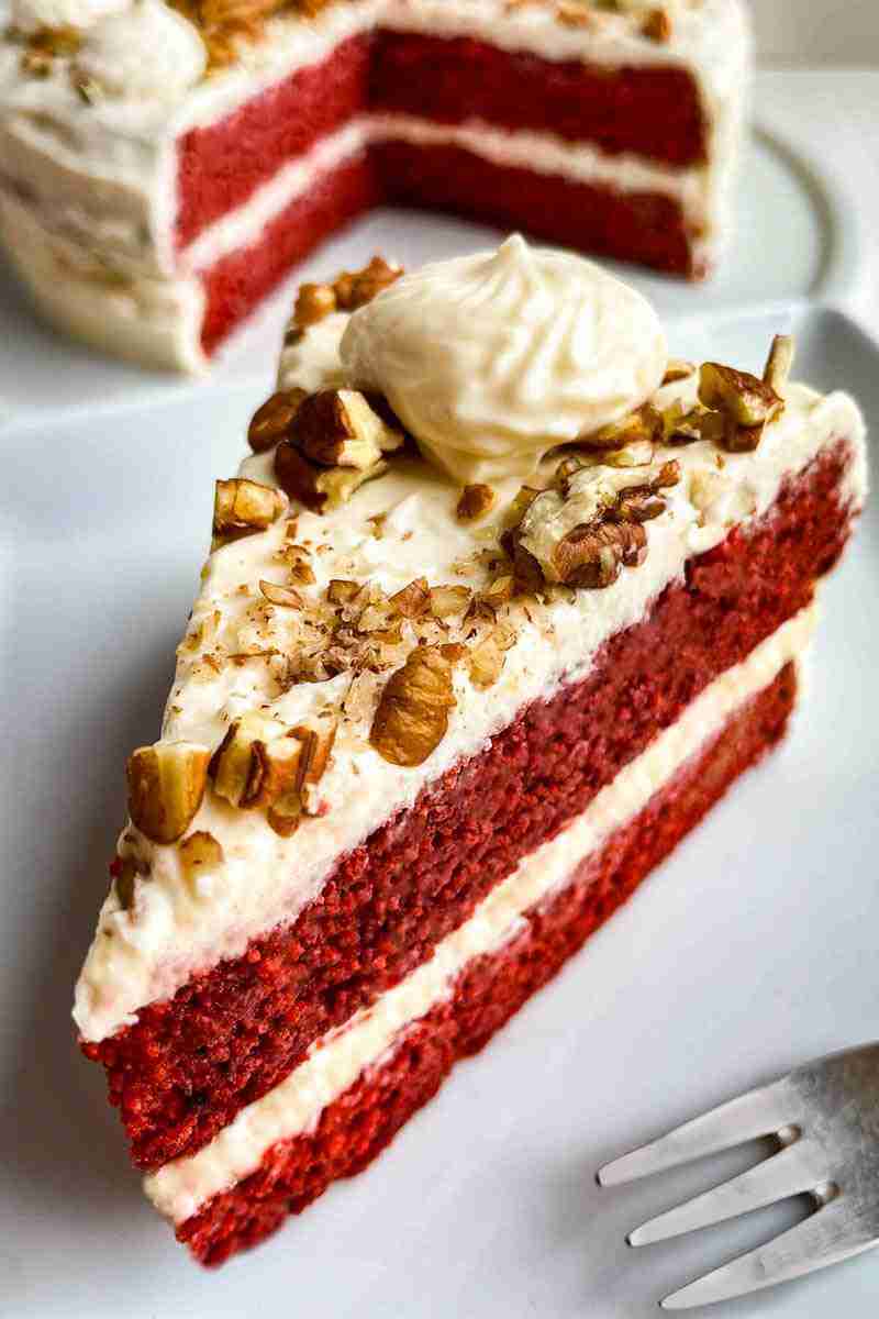 A slice of sugar free red velvet cake and a cake in the background.