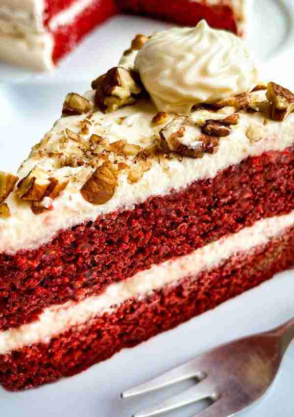 A slice of keto red velvet cake topped with cream cheese and pecans.