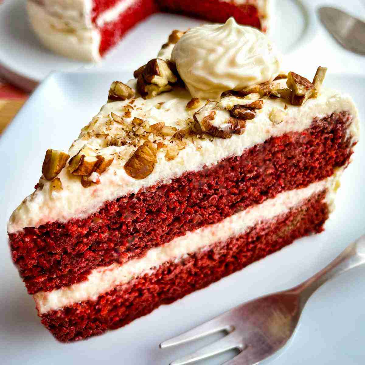 A slice of keto red velvet cake topped with cream cheese and pecans.