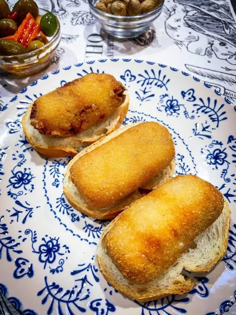 Three different croquettes: grapes and cheese, ham and cheese, and meat and cheese with a bowl of peanuts and a bowl of olives at Bar El Mercado.
