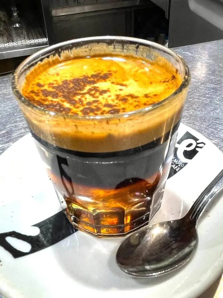 A cup of Cafe Cremaet which consists of espresso, rum, sugar, two coffee beans, and a sliver of lemon rind.
