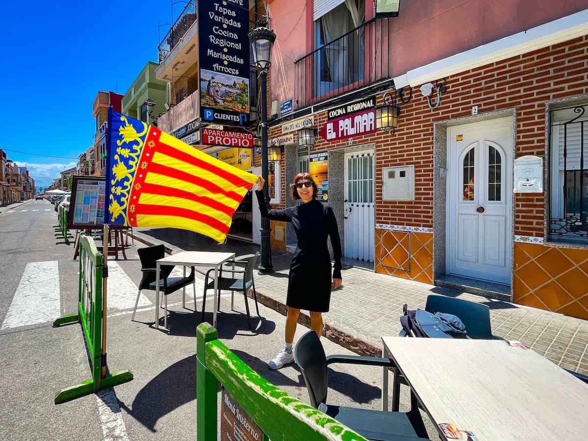 The author holds out the red, yellow and blue flag of Valencia in the village of El Palmar within Albufera Natural Park.