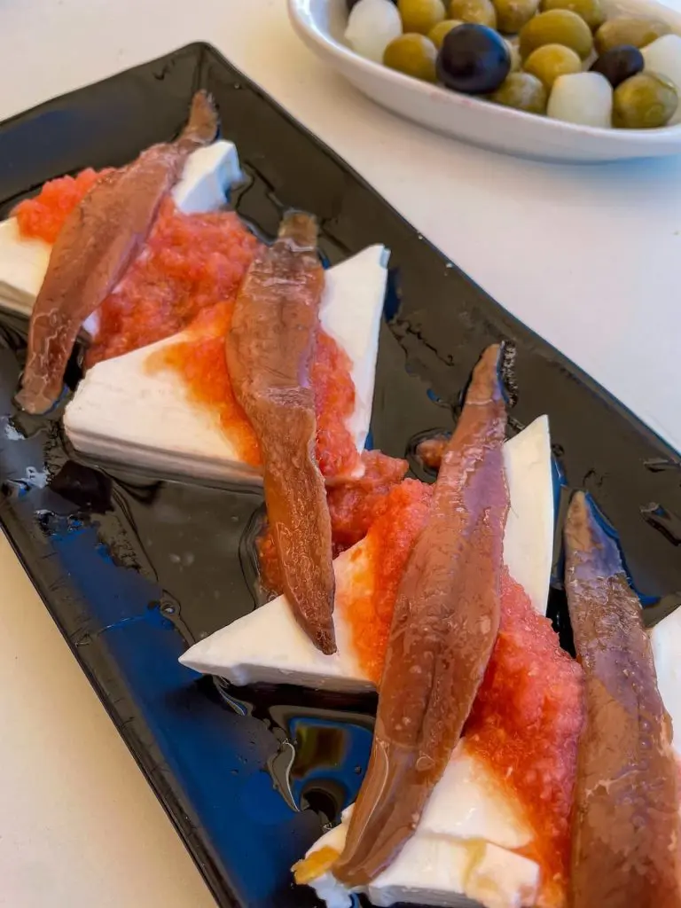 Food at Bodega La Pascuala, one of the best restaurants el cabanyal valencia: Goat cheese tapas topped with anchovies and tomato sauce and a bowl of olives.