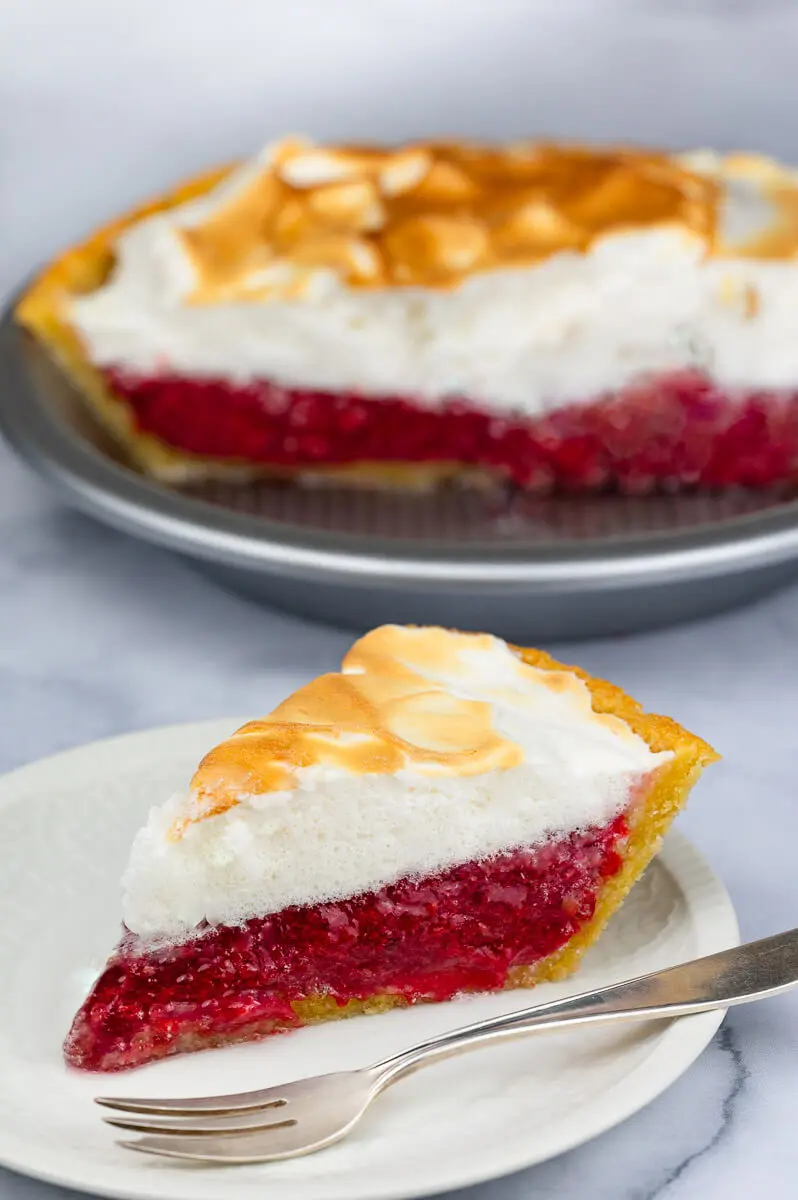 Sugar free cherry pie filling in a keto meringue pie topped with a monk fruit meringue. A slice sits next to the keto pie.