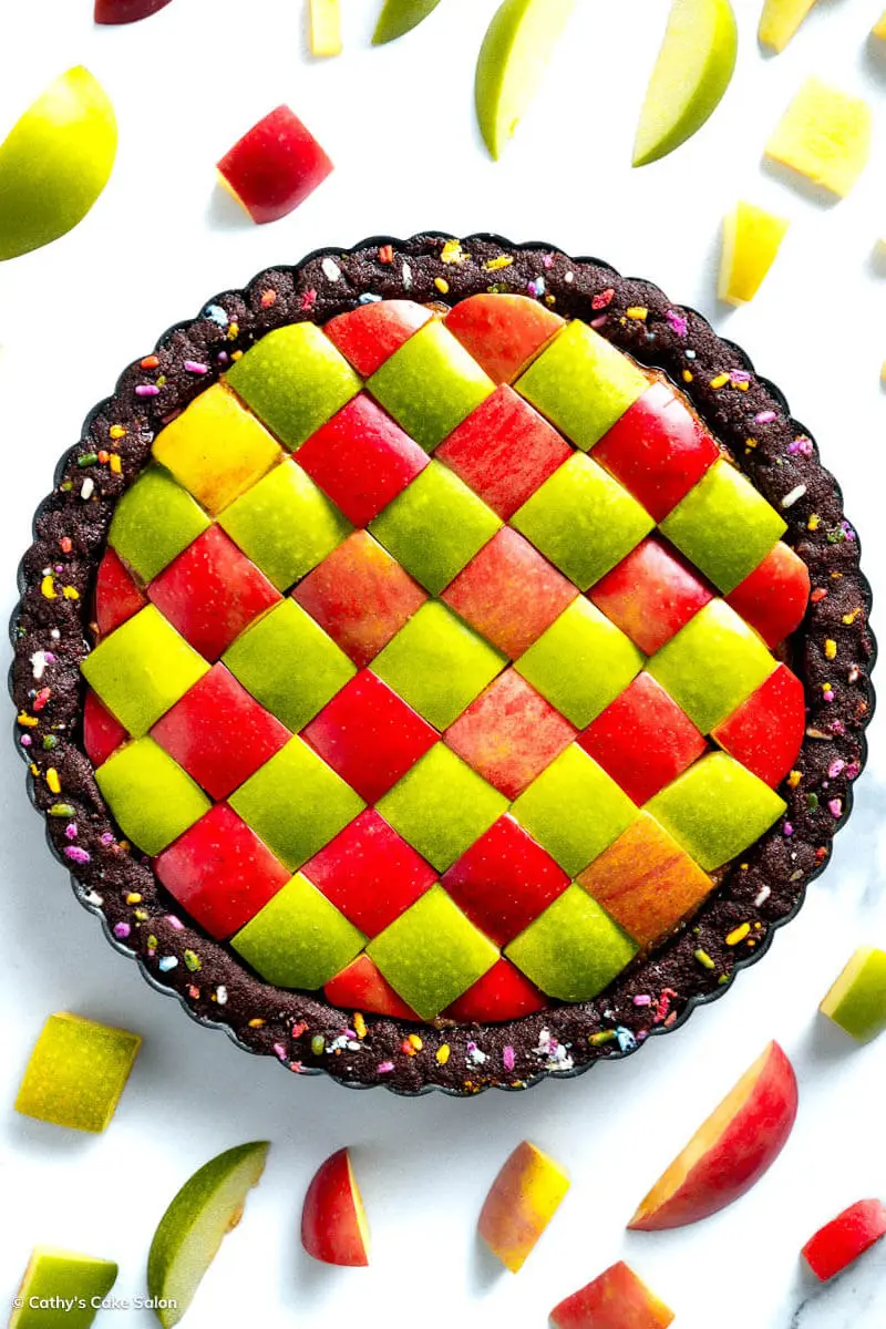 A vegan peanut butter chocolate pie. It features a keto chocolate pie crust filled with colorful funfetti sprinkles and holds a no-bake vegan peanut butter filling topped with geometric squares of red and green apples. This nondairy peanut butter pie is perfect for the Christmas holidays.
