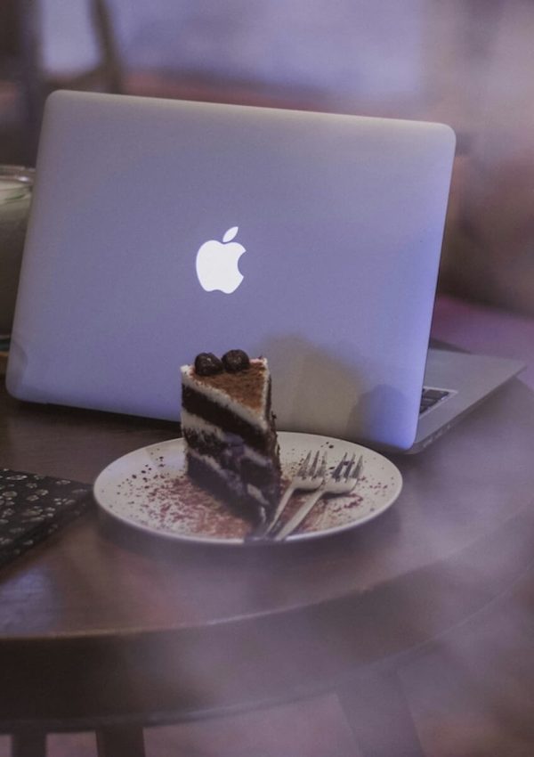 A portable work setup with a laptop next to a slice of healthy chocolate cake and a sugar free beverage.