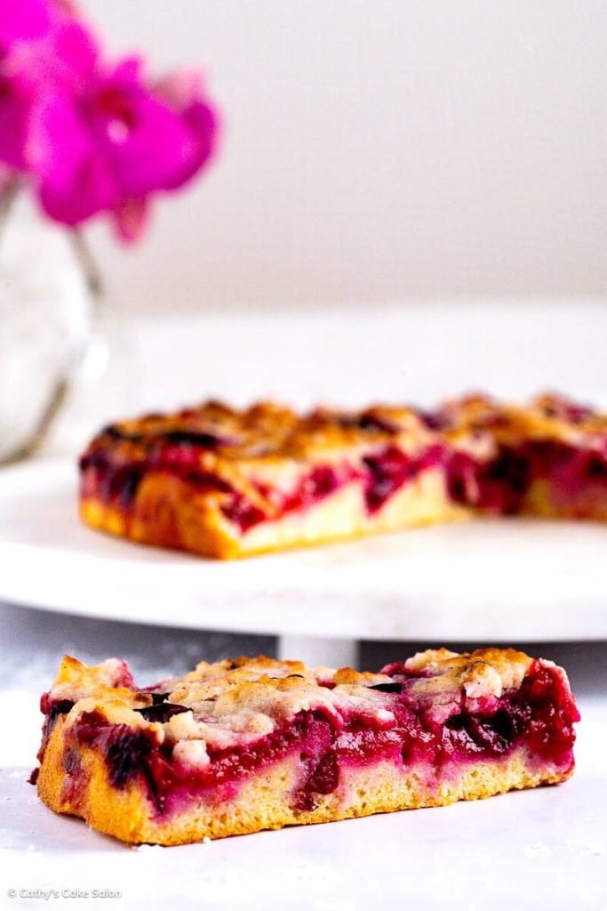 A slice of Sugar Free Plum Cake with the whole healthy plum cake in the background.