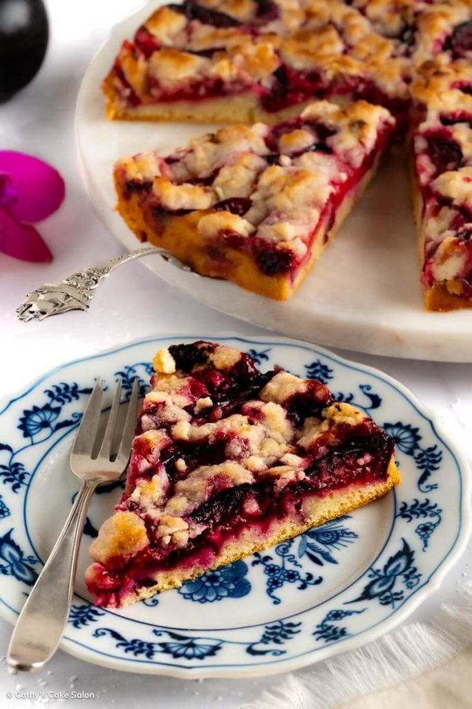 A slice of Sugar Free Plum Cake with the whole German plum cake in the background.