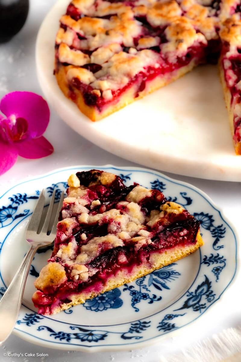 The result of my German plum cake recipe: a slice of sugar free plum cake topped with a buttery cinnamon streusel and the whole cake in the background.