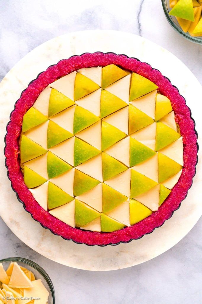 A gluten free apple tart in a fuchsia dragon fruit pie crust and topped with white chocolate and apple triangles.