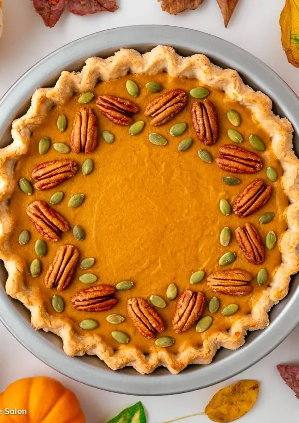 A vegan gluten free pumpkin tart in a silver pie pan and decorated with pumpkin seeds and pecans.