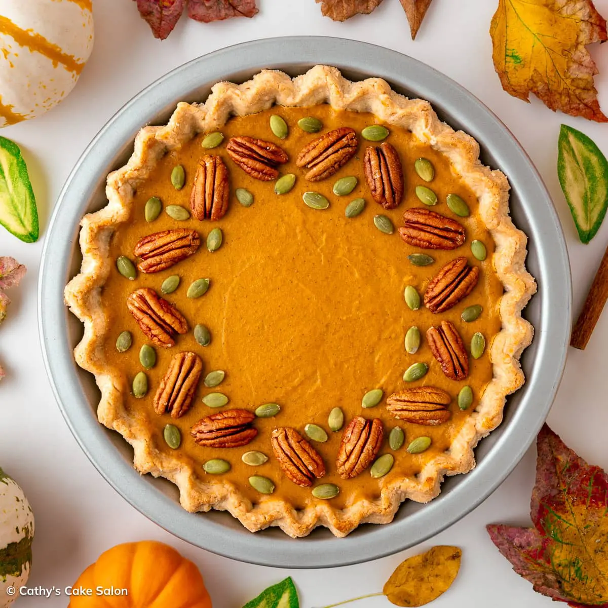 A vegan gluten free pumpkin tart in a silver pie pan and decorated with pumpkin seeds and pecans.
