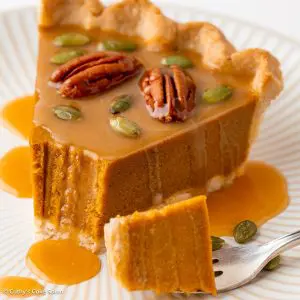 A slice of vegan no bake pumpkin pie and a piece on a fork. Caramel sauce drizzles down the slice.