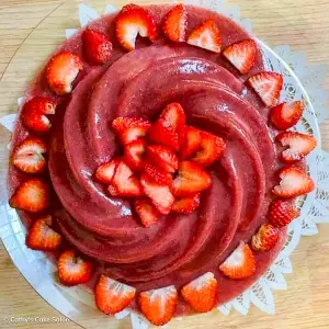 The result of this homemade strawberry jello recipe: a monk fruit sweetened jello cake in a pretty Nordic Ware Heritage Bundt Cake Pan. The cake is topped with fresh strawberries.