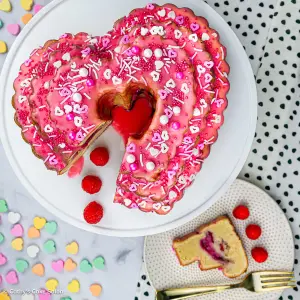A raspberry swirl bundt cake with fresh raspberries and white and pink Valentine's Day sprinkles.