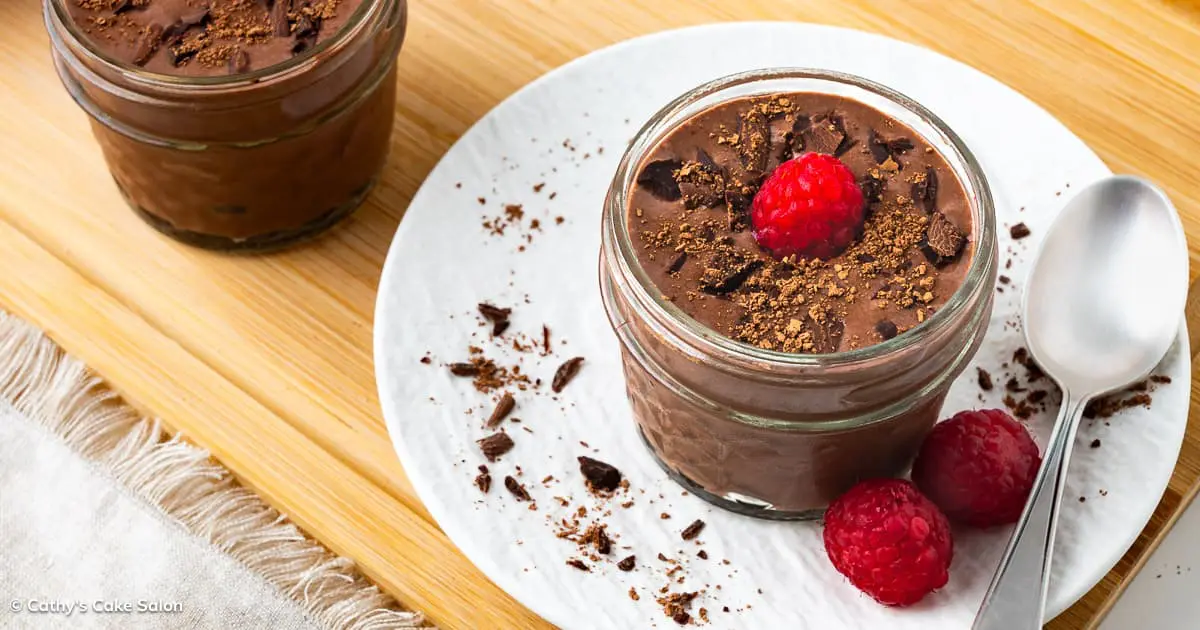 Two jars of cottage cheese chocolate mousse topped with cocoa nibs, cocoa powder, and a raspberry.