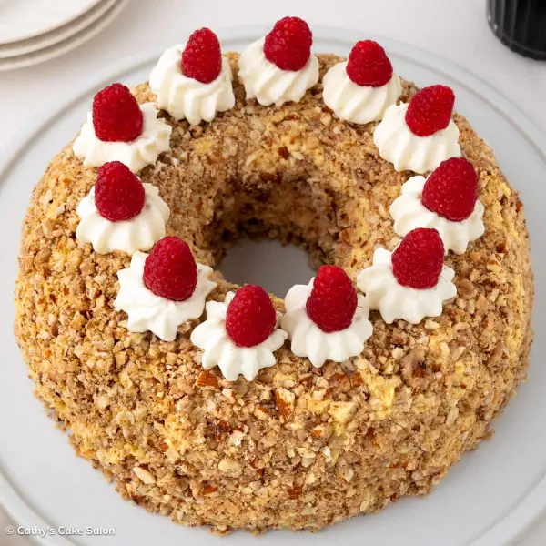 The German Frankfurter Kranz Cake, also called a Frankfurt Crown Cake, is coated with caramelized almond brittle and topped with whipped cream and raspberries.
