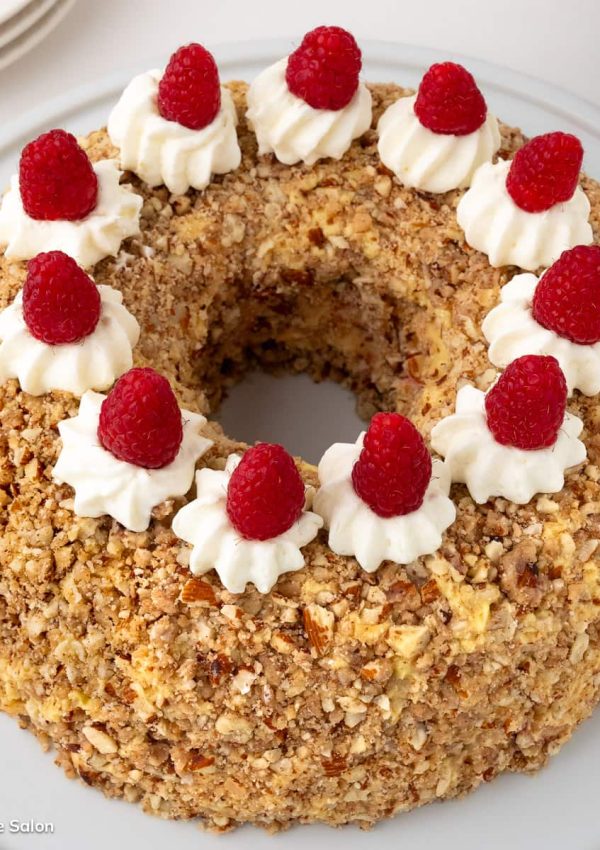 The German Frankfurter Kranz Cake, also called a Frankfurt Crown Cake, is coated with caramelized almond brittle and topped with whipped cream and raspberries.