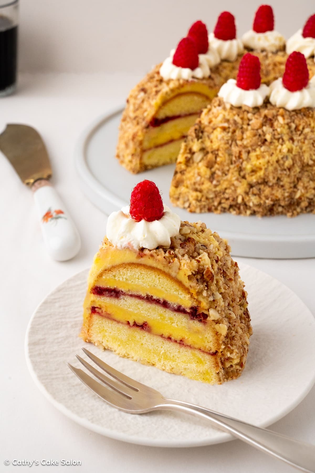 The result of this easy German crown cake recipe: a slice of Frankfurter Kranz cake with layers of raspberry preserves and buttercream next to the whole cake.