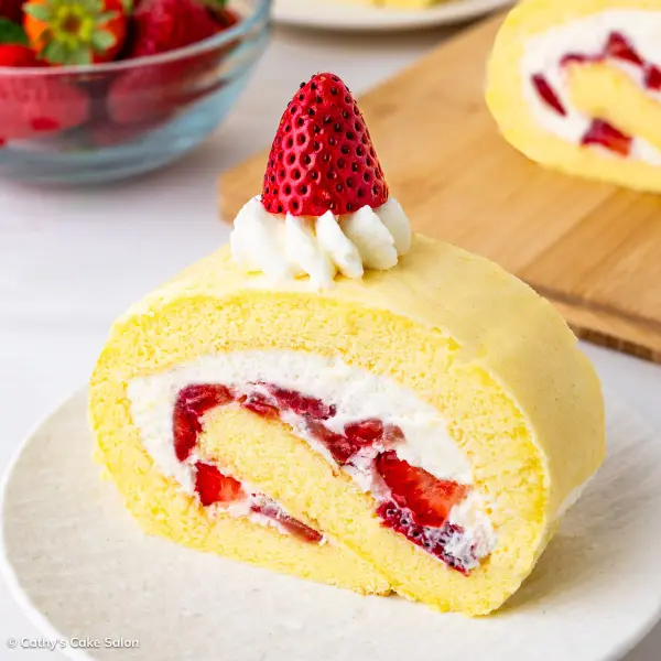 The result of this Japanese strawberry roll cake recipe: a slice of strawberry roll cake topped with whipped cream and a fresh strawberry.