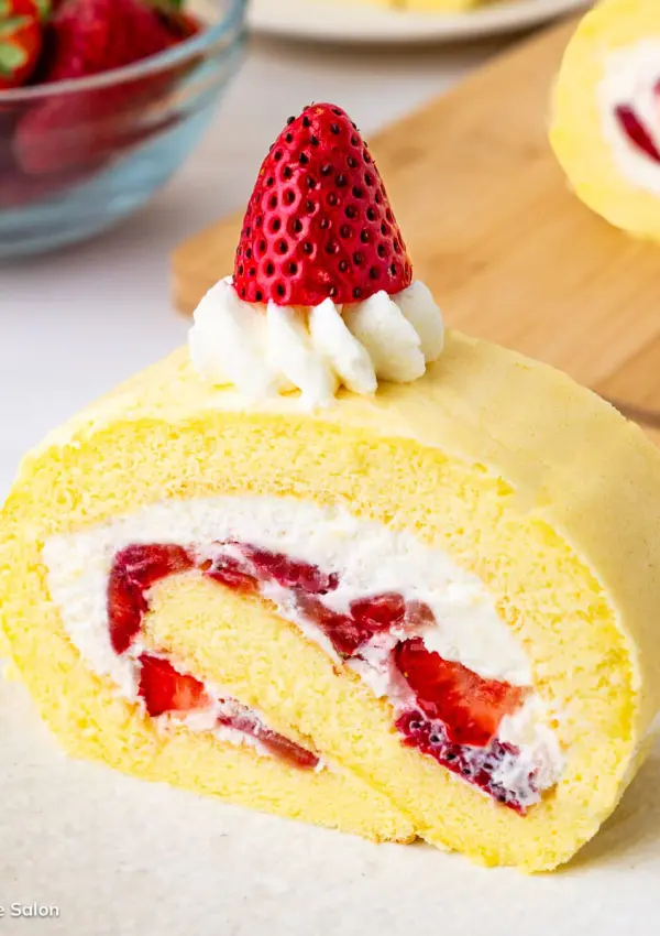 The result of this Japanese strawberry roll cake recipe: a slice of strawberry roll cake topped with whipped cream and a fresh strawberry.