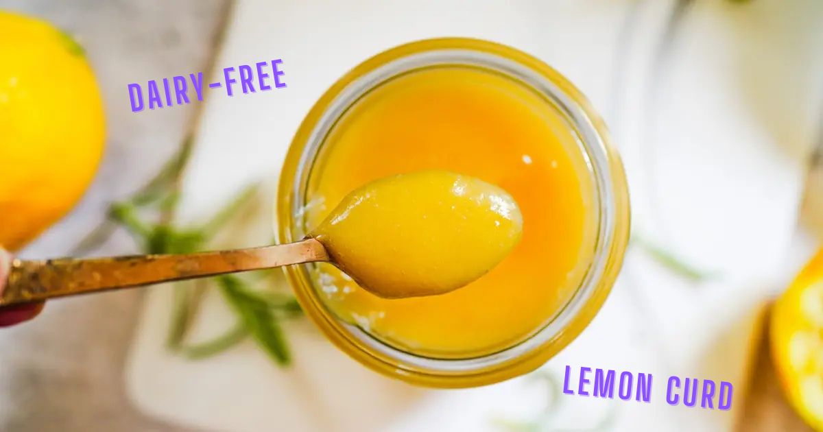 Dairy free lemon curd in a glass jar with a spoon plunged into the thick curd.
